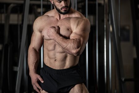 handsome young bearded man in sport trunks showing strong muscle of his perfect body physique in fitness gymの写真素材