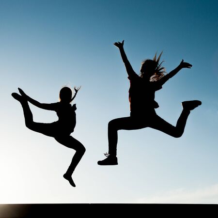 two young active girls jumping on blue sky backgroung outdoor leisure lifestyleの写真素材