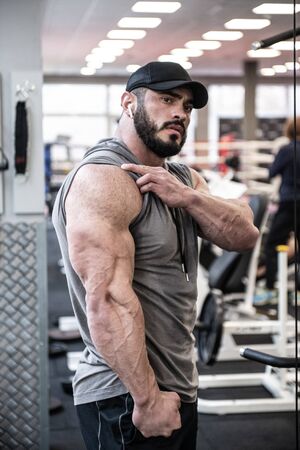 strong young bearded man showing big triceps muscle during posing in sport gym after hard workoutの写真素材