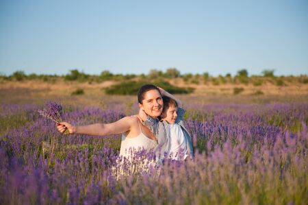 happy smiling family caucasian beautiful mother and embracing small kid in summer blooming flower field during leisure vacationの写真素材