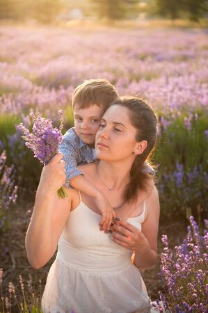 happy caucasian family cute little boy hugging his young beautiful mother with bouquet of lavender in summer flower fieldの写真素材