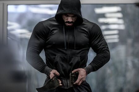 strong young bearded mighty man in hoodie wearing powerlifting belt for heavy hardcore weight training workout indoors sport fitness gymの写真素材