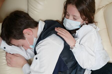 coronavirus covid-19 epidemic outbreak quarantine concept of two kids in school clothes lying sleeping on sofa suffering from painの写真素材