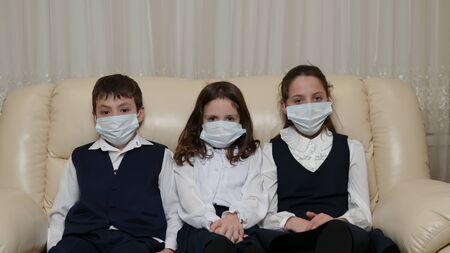 three little sick kids in school uniform wearing medical mask sitting at home during coronavirus covid-19 epidemic outbreak quarantineの写真素材