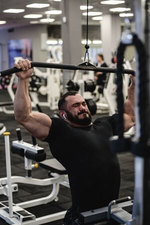 training stress of young bearded man during heavy workout in sport club gym with grimace of effort...
