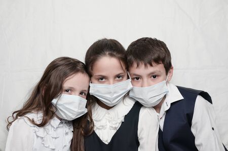 family of three little kids in medical masks and school uniform during coronavirus COVID-19...