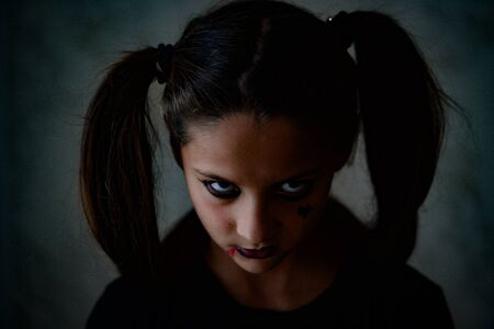 young little caucasian girl with pigtails with dark gothic makeup looking angry during Halloween holiday party looks like movie characterの写真素材