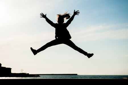 healthy young girl jumping high in air in city with sea in summer outdoorsの写真素材