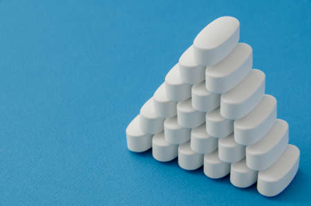 pyramid from many white vitamin drugs medication tablets on blue pure surface with copy spaceの写真素材