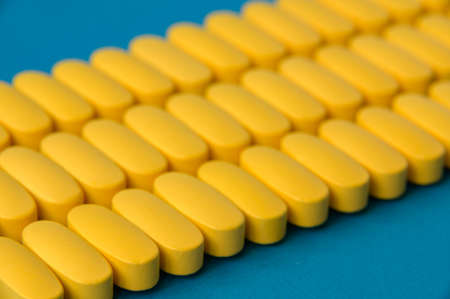 pharmacology industry produce concept of many rows of yellow pills tablets of vitamin drugs on blue surfaceの写真素材