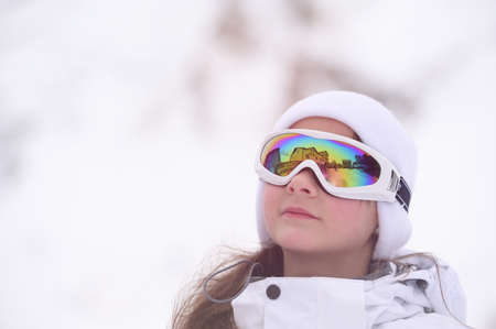 beautiful little girl in ski goggles and wool hat on white snow background in mountains with copy spaceの写真素材