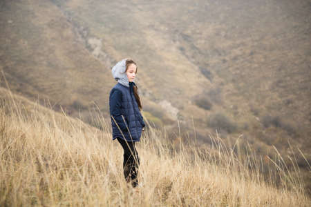 one lonely small girl in hoodie standing in mountains with hands in pocket during leisure recreation hike activityの写真素材