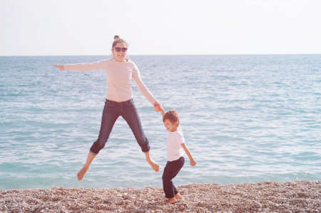 young active family of mother and child jumping on sea spring beach during outdoor leisure activityの写真素材