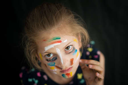 state of mind concept of beautiful little caucasian girl with face painted with colorful paintの写真素材