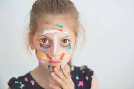 beautiful little serious caucasian girl with face painted with colorful paint with copy spaceの写真素材