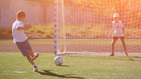 active little kid kicking ball to football gate with boy goalkeeper on soccer green fieldの写真素材
