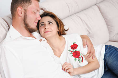 beautiful young couple male and female sitting on couch looking at each otherの写真素材