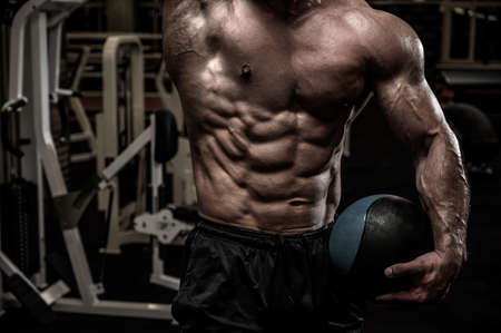 strong physique body torso of strong young male with perfect abdominal muscle holding heavy training ball in gymの写真素材