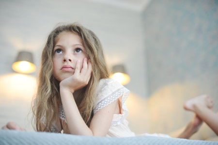 pretty lazy idle little girl with long hair watching TV lying in bedroomの写真素材