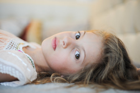 mind imagination concept of beautiful little girl lying in bed watching in camera with big eyes with interestの写真素材