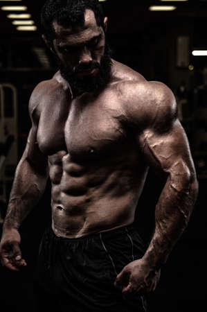 strong sport athlete male with beard and perfect physique body in dark fitness gymの写真素材