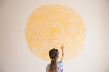 creative concept of little girl pointing finger at yellow circle sun painted on wall with copy spaceの写真素材