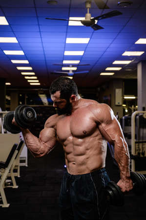 muscular bearded strong caucasian man lifting dumbbells during heavy workout train in sport gymの写真素材