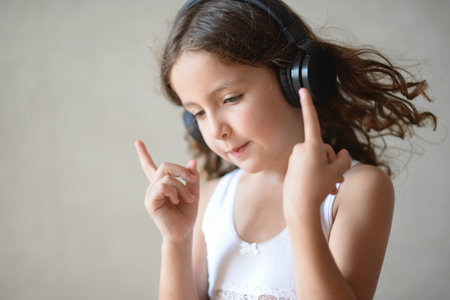beautiful little curly girl in headphones listen music conducting with hands and fingers during leisure indoors activity hobby lifestyleの写真素材