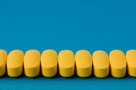 row of yellow medical pills tablets on blue surface with copy spaceの写真素材