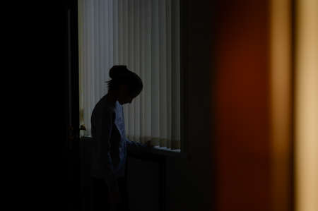 trouble and problem concept of domestic violence upset sad little girl on blue window background in sunset home roomの写真素材