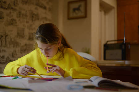 caucasian little girl in yellow shirt hoodie working on creative art task project with pencil drawing at home indoor room at nightの写真素材