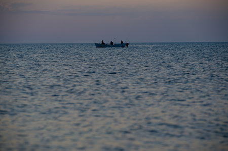 group of people fishermen with rod on float boat on sea horizon on dusk twilight during fishing with copy spaceの写真素材