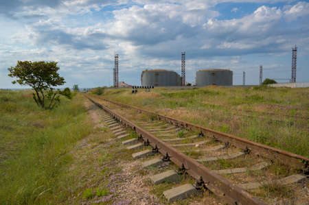 ecology environment concept of old rusty railroad railway and oil tanks cistern on background with cloudy blue skyの写真素材
