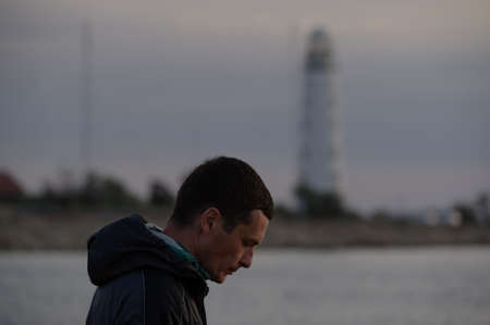 state of mind feel emotion concept of upset sad man head down near sea coast with lighthouse on background at dusk timeの写真素材