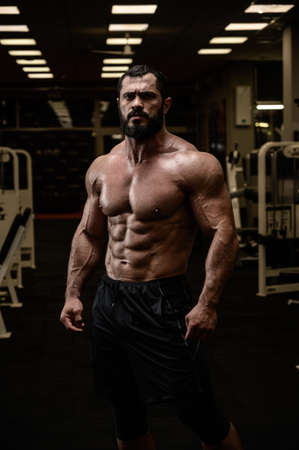 strong young male with beard and perfect fitness abdominal muscles in sport gym in nightの写真素材