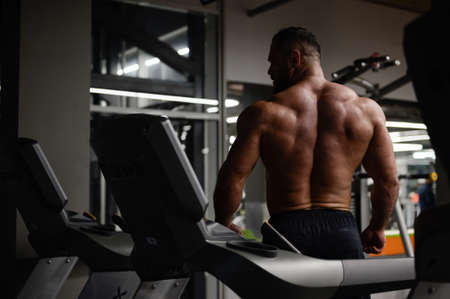 strong young bearded male athlete looking over shoulder in sport gym among exercise equipmentの写真素材