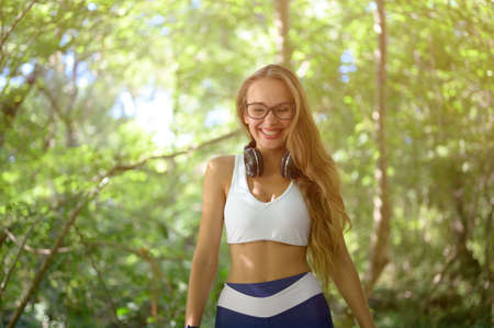 happy laughing pretty young girl in sportswear and glasses with wireless headphones in green park during summer sport leisure recreation activityの写真素材