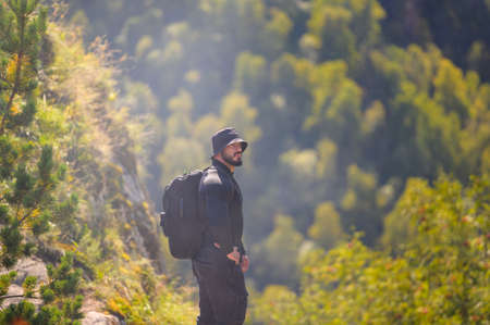 sport strong young bearded athlete male in black clothes with backpack during hiking in forest mountainの写真素材