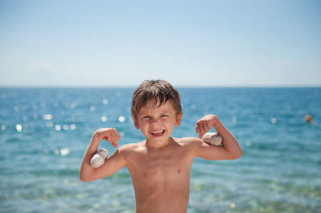 happy adorable little kid showing muscle with stones on biceps on sea backgroundの写真素材