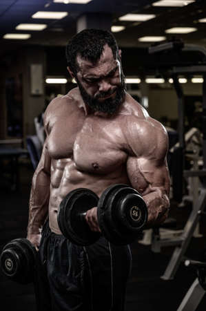 strong young bearded caucasian muscular man lifting heavy dumbbells in sport gym during fitness bodybuilding workout trainingの写真素材