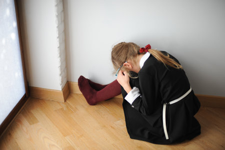 little upset school girl in black dress sitting on floor with head down on knee after education failの写真素材