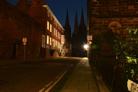 Old Lichfield street glows under lamplight, cathedral spires looming in shadowed distance.の写真素材