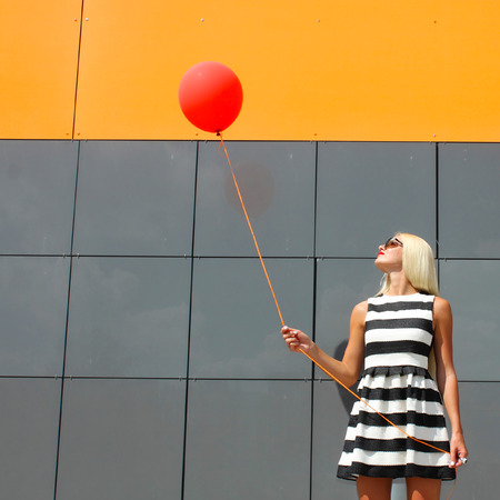 young happy trendy girl stands near a wall mirror with a red balloon. Outdoors, lifestyle. concept of happiness and joyの写真素材