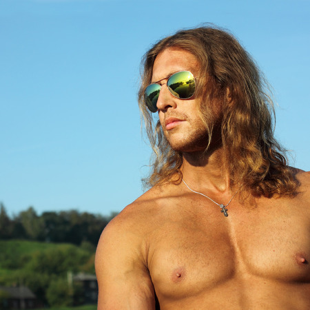 Portrait courageous unshaven man with long red hair and a cross on his neck on background of sky. like Jesusの写真素材