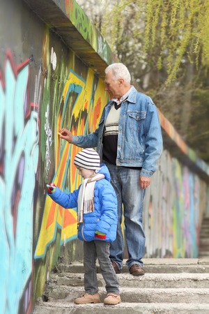 Grandfather and grandson paint graffiti on the wallの写真素材