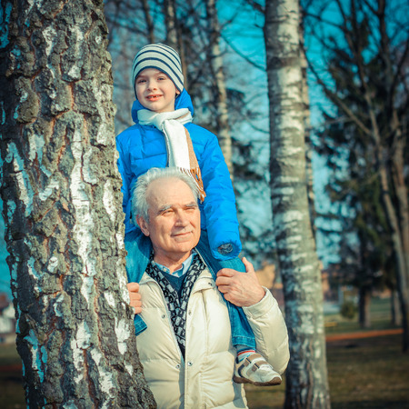Grandfather and grandson indulge. Grandfather Carrying Grandson On His Shoulders. The grandfather makes movies on old movie camera.の写真素材