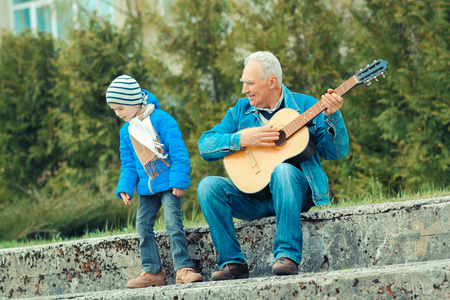 Grandfather and grandson playing guitar outdoorsの写真素材