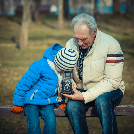 Grandfather and grandson are exploring vintage medium format cameras. Grandfather shows grandson retro cameraの写真素材