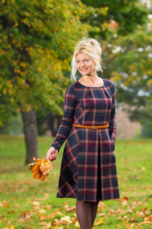 Beautiful mature blonde in checkered dress posing in the park. Portrait of a senior woman outdoors.の写真素材