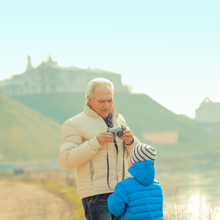 Grandfather and grandson are photographed on a vintage camera. Grandfather and grandchild in a landscapeの写真素材